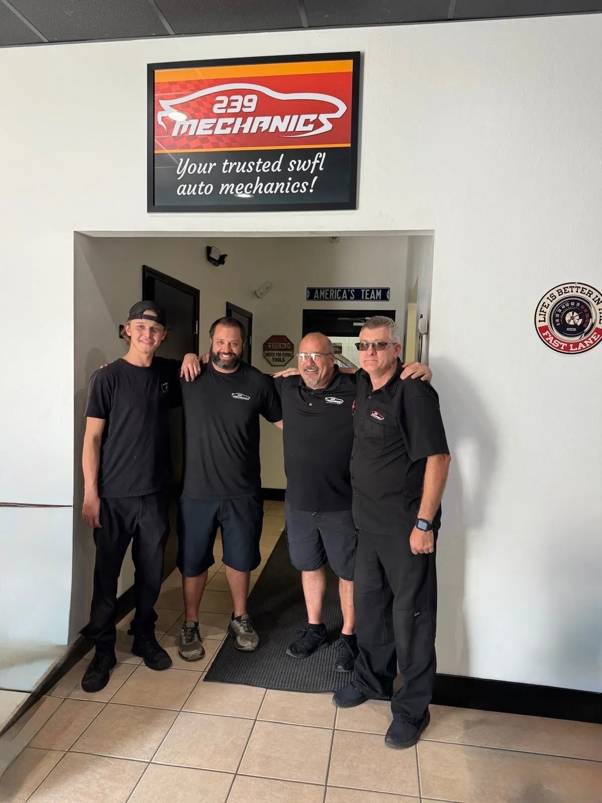 Four members of the 239 Mechanics team at the front entrance under the "Your trusted SWFL auto mechanics" sign
